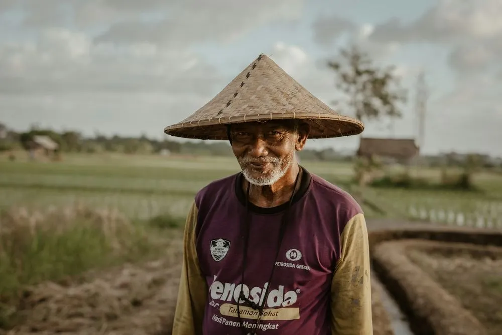 A smiling Balinese farmer in a straw hat at the edge of his fields