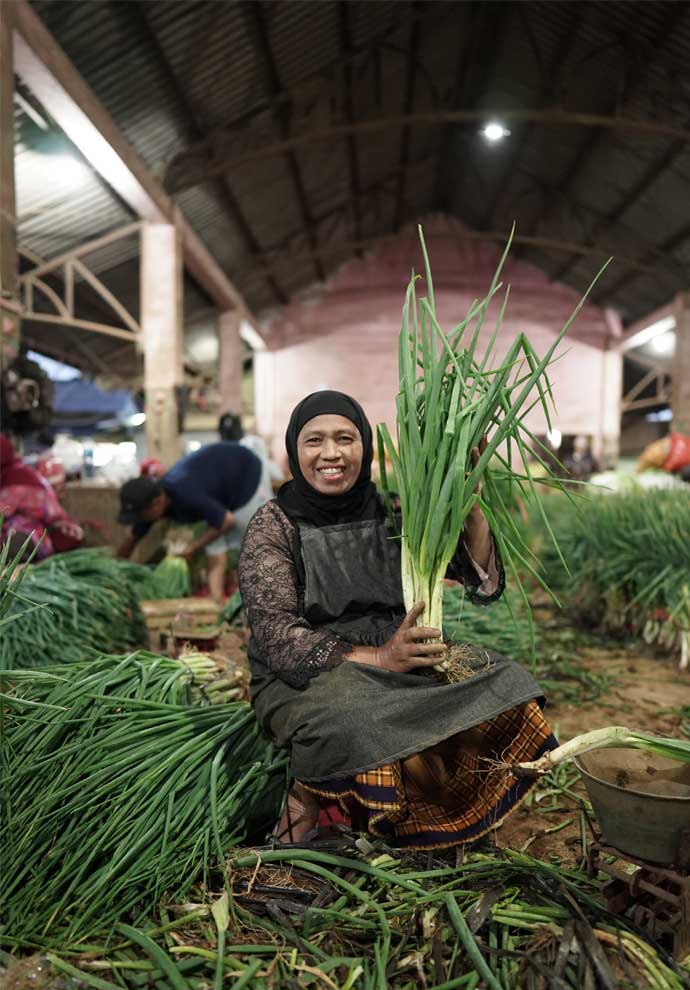 Seorang Ibu-Ibu Pedagang Sayuran Menunjukkan Hasil Pertanian yang Beliau Dagangkan